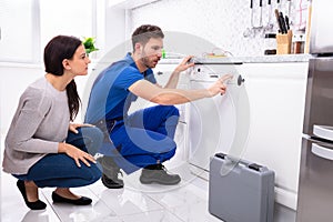 Serviceman Pressing Button Of Dishwasher In Kitchen