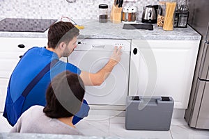 Serviceman Pressing Button Of Dishwasher In Kitchen