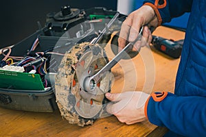 Serviceman stripping and removing wheels on robotic lawnmower, motorized lawnmower being serviced on a table after a year of use