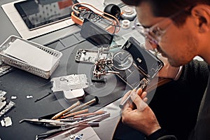 Serviceman uses magnifier and screwdriver to repair damaged smartphone in the workshop.