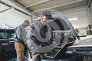 Servicemen completing car engine diagnostics with laptop in a repair shop