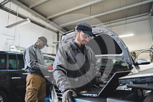 Servicemen making car diagnostics with laptop in a workshop