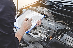 Services car engine machine concept, Automobile mechanic repairman checking a car engine with inspecting writing to the clipboard