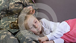 Servicewoman stroking sleeping daughter relaxing on sofa, family connection