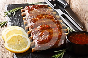 Serving BBQ pork ribs with chili sauce and lemon close up on a slate board. horizontal