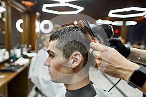 Serving client. Close up shot of barber drying hair of a young handsome guy visiting modern barbershop