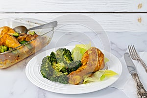 Serving dinner. Close-up view of a plate with an oven-baked chicken drumstick and broccoli served with fresh lettuce