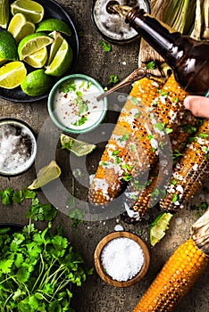 Serving grilled corn cob with fresh herbs,lime,beer at picnic, top down table view