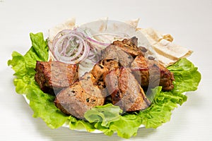 A serving of grilled meat lies on lettuce, with onion rings and pita bread