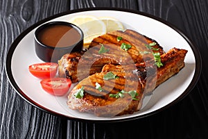 Serving grilled pork cutlet with tamarind sauce, lemon and fresh tomatoes close-up on a plate. horizontal