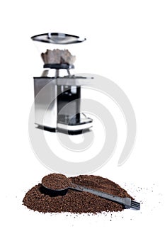 Serving measuring scoop full of coffee grounds in a hill of coffee with an espresso machine out of focus in the background