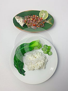 Serving rice, pakcoy boiled, bitter bean, and steamed fish yellowtail scad with matah chili sauce on a plate