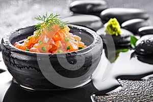 Serving of salmon tartar in a black stone bowl on a background with black stones, Zen style