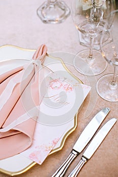 Serving the table with a porcelain dish with a pink napkin, menus, knives and glasses for wine