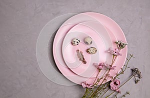 Serving of two pink plates with beautiful small quail eggs, a feather and a branch of a wildflower