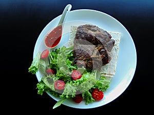 Serving white plate with crispy fried meat, vegetables, thin bread and sauce on black surface