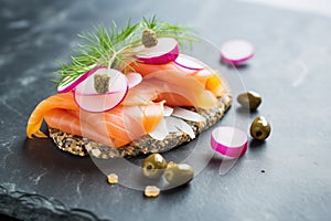 sesame bagel, lox, red onions, and capers, on a slate