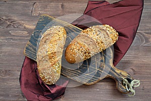 A sesame buns on a wooden cutting board and grenadine napkin on wooden table top view