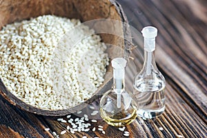 Sesame oil in a glass bottle and heap sesame seeds in coconut shell on wooden rustic table. Selective focus.