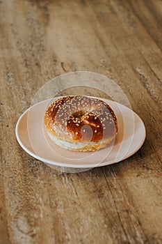 A sesame seed bagel on a pink plate on a wooden table and plate is on a slightly angled table