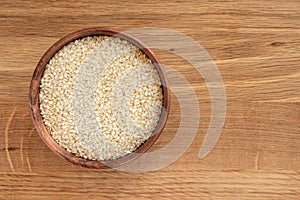 Sesame seeds in bowl on wooden background, top view