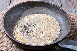 Sesame seeds are fried in the pan on a wooden table