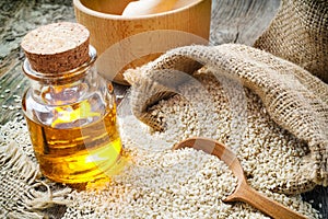 Sesame seeds in sack and bottle of oil on rustic table photo