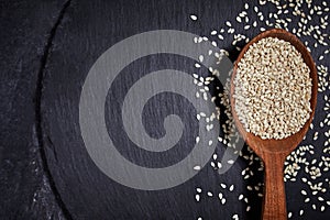 Sesame seeds and a wooden spoon with black slateboard on a dark table. Healthy food and drink concept. Top View