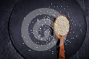 Sesame seeds and a wooden spoon with black slateboard on a dark table. Healthy food and drink concept. Top View