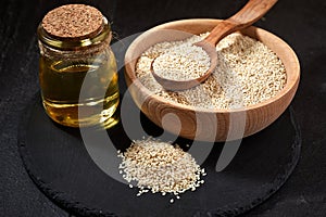 Sesame seeds and a wooden spoon on a dark table. Black slateboard with wooden bowl and bottle of oil. Copy space