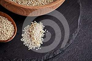 Sesame seeds and a wooden spoon on a dark table. Black slateboard with wooden bowl. Copy space