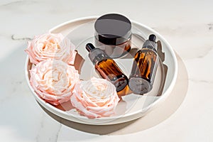 Set of amber glass cosmetic bottles on ceramic tray. dropper bottle and cream jar package. Skincare beauty products
