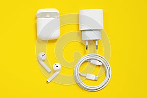 Set of Apple devices, white wireless AirPods with box, power plug and wire lightning to usb type c, on yellow background