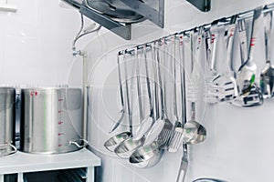 A set of basic kitchen utensils hangs on the wall with an aluminum shelf for many lids photo