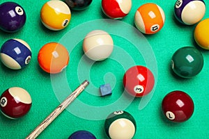 Set of billiard balls with cue and chalk on green table, flat lay