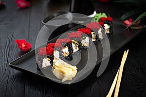 set of black sushi rolls on a black plate on a black wooden background
