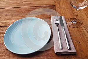 Set of blue empty plate, napkin, fork and knife on brown wooden table in restaurant