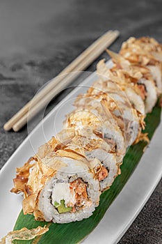 Set of bonito rolls with grilled salmon, avocado, tuna shavings and green bamboo leaf in a white ceramic plate with chopstick on a