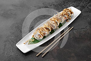 Set of bonito rolls with grilled salmon, avocado, tuna shavings and green bamboo leaf in a white ceramic plate with chopstick on a