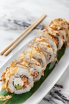 Set of bonito rolls with grilled salmon, avocado, tuna shavings and green bamboo leaf in a white ceramic plate with chopstick on a