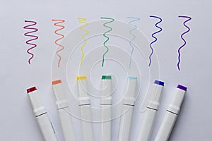 A set of bright multi-colored felt-tip pens or markers lie on white background sheet of paper, with samples of drawing. Creativity