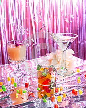 Set of bright sweet cocktails on a pink shiny background with glitter and soap bubbles.