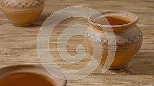 Set of brown pots handmade from clay with ornament on rustic wooden table. Earthenware for drink and food. Kitchen