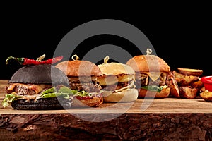 Set of burgers with meat, cheese, tomatoes, mayonnaise on wooden table, black background. Space for text.
