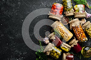 Set of canned vegetables and mushrooms in glass jars. Set of pickled food on black stone background.