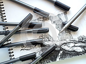 A set of capillary pens is laid out on a landscape sheet. The process of drawing graphics with a black capillary pen.