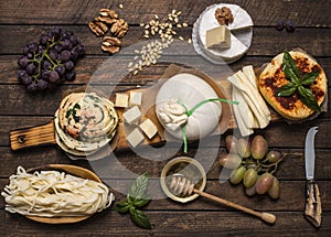 A set of cheeses. Halumi, cheese sticks, Suluguni, Camembert,  fresh soft white burrata cheese ball, mozzarella on a wooden board