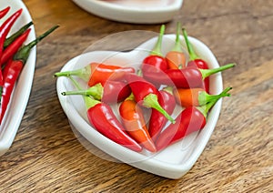 Set of chili peppers mini pods in a plate heart close-up on a wooden background