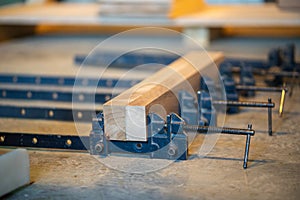 Production process at carpentry workshop, clamps for compression and wooden block laying on table.