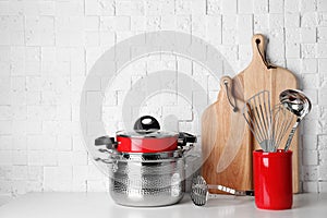 Set of clean cookware and utensils on table against white wall